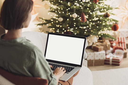 Young woman using laptop computer with blank empty mockup screen during Christmas holidays at home, Online shopping at winter holidays, ordering Christmas gifts, Website template.