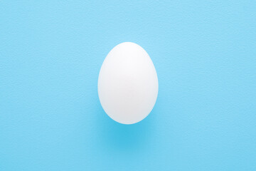 White egg on light blue table background. Pastel color. Closeup. Top down view.