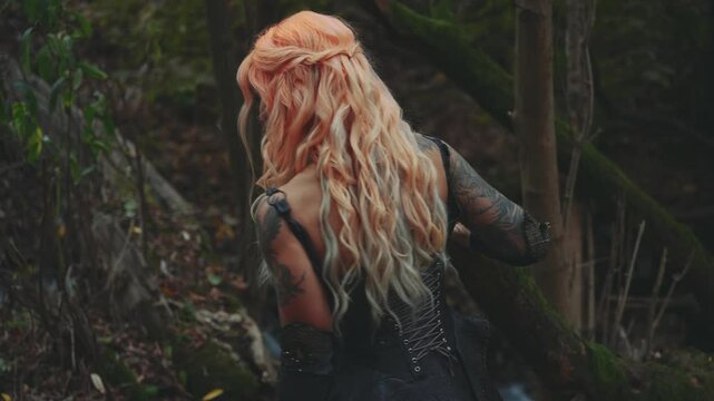 fantasy woman warrior queen holding knife blade dagger. Sexy girl elf in dark night forest walking by river water stream nature. Black dress, beautiful lady unrecognizable face blond hair back view 4k