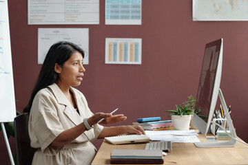 Side view of confident female teacher of English language looking at student on computer screen during explanation of rules