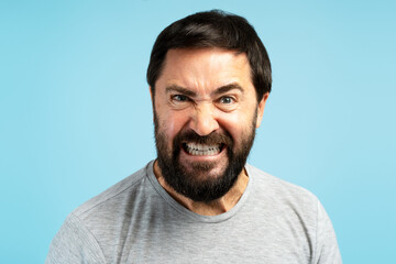 Fototapeta premium Angry man showing teeth and grimacing on blue background