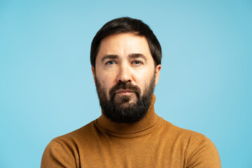 Serious man with beard and turtleneck posing on blue background