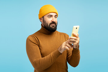 Bearded man using smartphone on blue background, modern man browsing internet on mobile phone