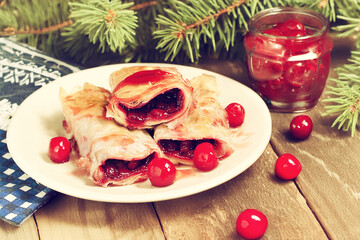 A plate of sour cherry filo pie with syrup poured over it. Fresh cherries surround the rolls, adding vibrant color and a seasonal touch. In the background, there's a jar of candied cherries.