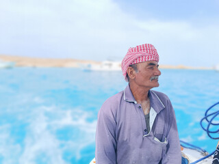 Old Sailor in the Sea Riding and Sailing with his Boat An old sailor with a white with a white mustache who is wearing a Bedouin Scarf on his head