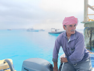 Old Sailor in the Sea Riding and Sailing with his Boat An old sailor with a white with a white mustache who is wearing a Bedouin Scarf on his head