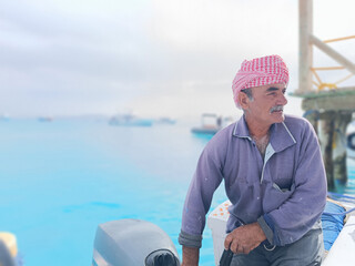 Old Sailor in the Sea Riding and Sailing with his Boat An old sailor with a white with a white mustache who is wearing a Bedouin Scarf on his head