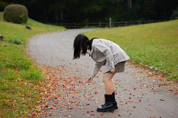秋の公園で赤色の紅葉の落ち葉を拾う女子高校生の姿