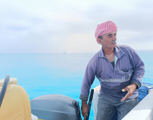 Fototapeta premium Old Sailor in the Sea Riding and Sailing with his Boat An old sailor with a white with a white mustache who is wearing a Bedouin Scarf on his head