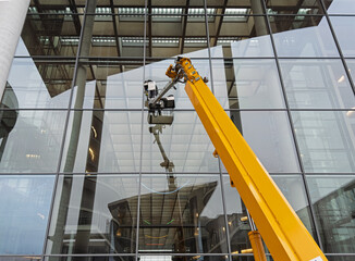 Cleaner worker using a cherry picker to clean a glas facade of a contemporary office building