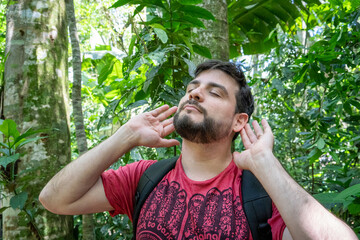 Hombre escuchando atentamente los sonidos de la naturaleza, estando en un bosque tropical lleno de...