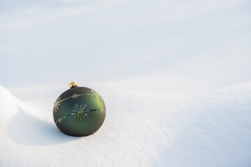 A green bauble with gold decorations lying on white natural snow on a sunny frosty day.