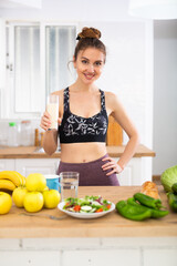 Happy slim sporty girl drinking yogurt in home kitchen