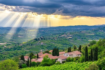 Obraz premium Beautiful Scenic View of Italian Countryside with Vineyards, Rolling Hills, and Sunlight Streaming Through Clouds in Springtime Landscape