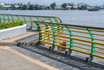 A vibrant waterfront promenade featuring colorful yellow and green railings beside a river