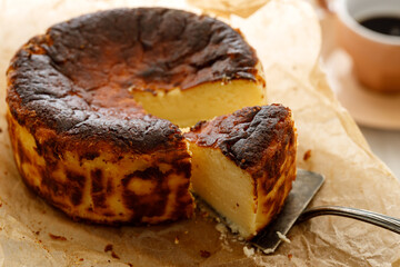 Naklejka premium Traditional Basque cheesecake with a cut portion on baking paper, close up view