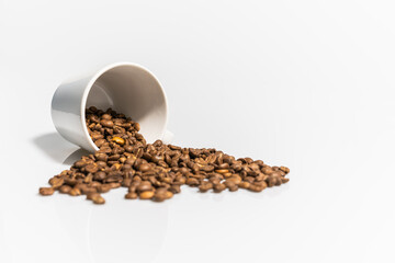 Image of coffee beans spilling from a white coffee cup on a white background.