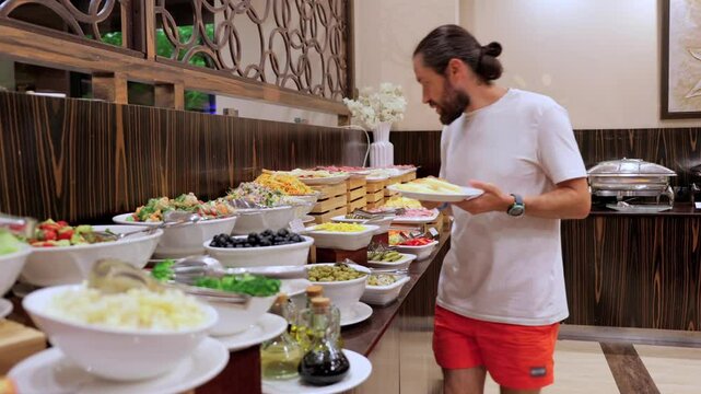 A man chooses food at a hotel restaurant for breakfast in a self-service setting. This video showcases the abundance of delicious breakfast options available for guests