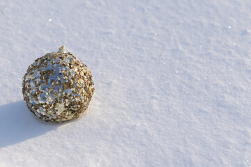 A golden bauble with gold decorations lying on white natural snow  on a sunny frosty day.