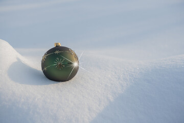 A green bauble with gold decorations lying on white natural snow  with star on a sunny frosty day.