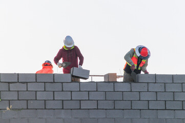 A crew of block masons laying concrete blocks to build an exterior wall of a commercial building