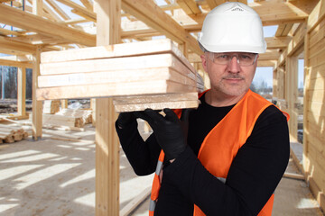 Man builder smiles. Guy building house from wooden planks. Loader works at construction site....