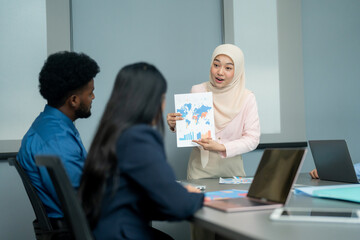 Professional in a hijab presenting charts and global data to colleagues during a business meeting in a modern office setting.