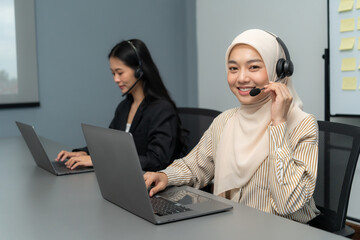 Two diverse customer service representatives working at desks with laptops and headsets, providing professional assistance in a modern office.