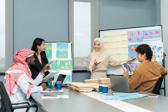 Diverse team of professionals in a meeting room presenting and discussing eco-friendly business solutions with charts and visual aids.