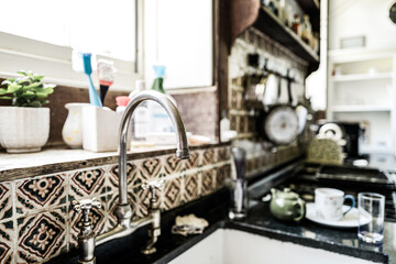 Shallow focus of a mixer tap spout seen in a large kitchen of a private mansion in the UK. The kitchen is set slightly below ground level of this large, old house.