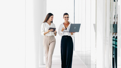 Two business women in the lobby of a modern office are discussing the work of a new project. Business, technology and teamwork concept.