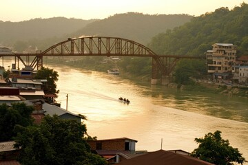 Fototapeta premium A scenic view of a river with a bridge in the background and a boat in the foreground, with a town on the right side of the river and hills in the background, during a sunset.
