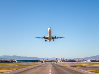 Obraz premium Airplane taking off from the runway against a clear blue sky with a distant city skyline and mountains visible in the background