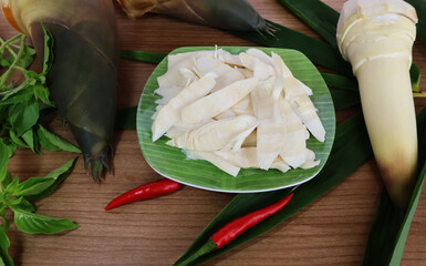 Cut bamboo shoots onto a green plate. Place ripe red chilies on a wooden table along with basil leaves. and the shoots and leaves are grouped together.

