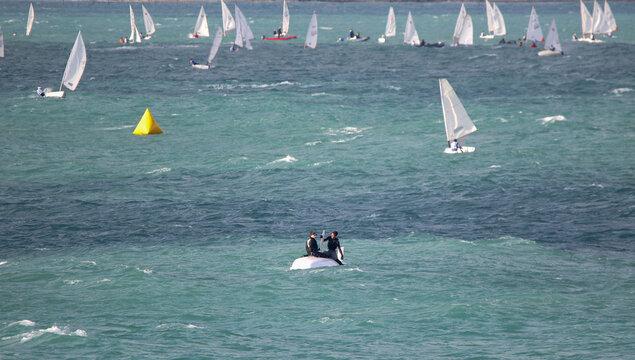 Yachtsmen sit on the hull of a capsized yacht and wait for help at sea in strong winds