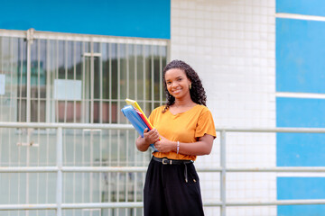 Estudante brasileira negra parada em frente à entrada da faculdade. Ela está sorrindo e feliz por ingressar no ensino superior. Conceito de universitários iniciando as aulas. 