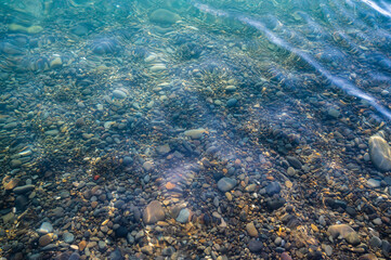 Underwater pebble backgrounds. Colorful stones sea bottom in the sun rays. View from above through clear water. Seascape wallpaper texture. Soft focus.