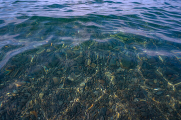 Underwater pebble backgrounds. Colorful stones sea bottom in the sun rays. View from above through clear water. Seascape wallpaper texture. Soft focus.