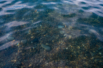 Underwater pebble backgrounds. Colorful stones sea bottom in the sun rays. View from above through clear water. Seascape wallpaper texture. Soft focus.