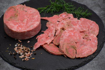 Vegan ham made of wheat gluten, shaped and cooked in a ham press. Sliced, slate board.