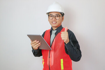Portrait of happy young handsome Indian male civil engineer or architect wearing helmet at construction site