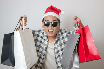 An excited young man dressed as santa clause carrying many shopping bags, isolated on white background. Concept for Christmas Holidays and New Year Party.