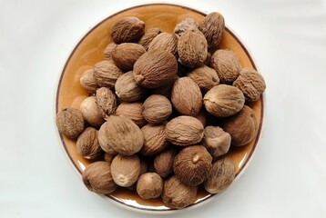 Bunch, heap or pile of organic and fresh cracked dry brown myristica or nutmeg seeds inside a bowl with a white background for copy space. Ayurvedic medicine spice ingredient. Extreme closeup top view