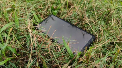Black smartphone or touchscreen mobile phone with silicone cover protection fall on the park green...