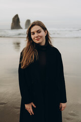 An incredibly beautiful girl with loose hair in a black coat on the ocean shore.