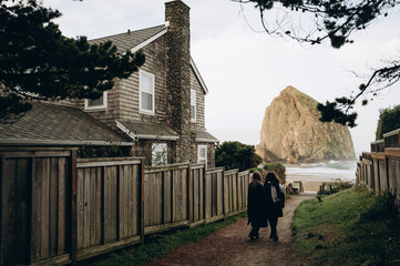 Two girls walk to the ocean with rocks along a path surrounded by a wooden fence.