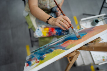 Female artist painting on canvas using paintbrush in art studio