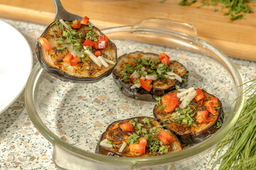 A Cook places fried eggplant slices sprinkled with sweet pepper, garlic and dill in a glass dish for further fermentation. Home cooking. Close-up