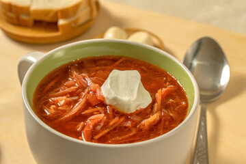 Vegetable soup with sour cream in a plate with bread, salt and garlic on a wooden background. Cabbage soup. Borsch
