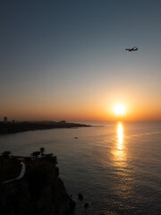 Tranquil coastal landscape at sunrise, featuring a cascading waterfall flowing gently into the calm sea. Warm golden hues of the rising sun reflect on the water, plane is flying